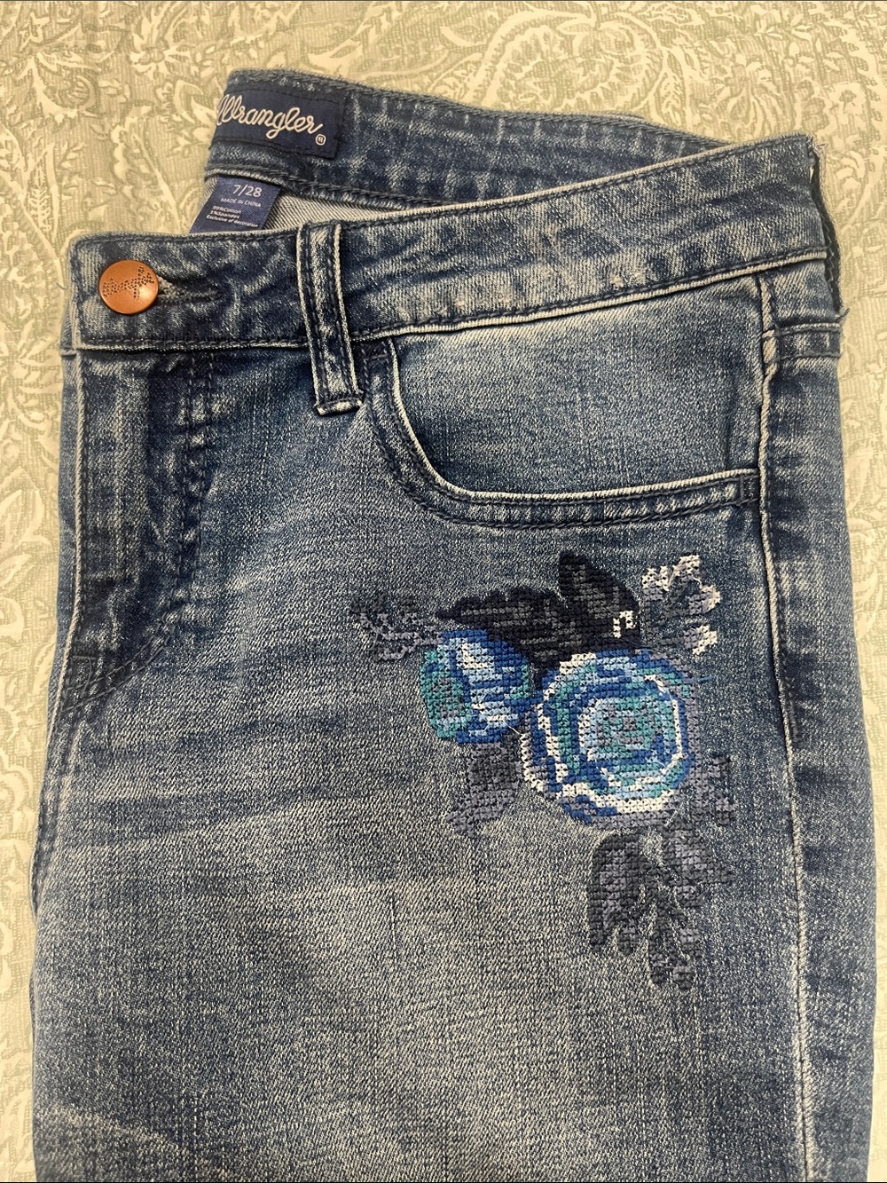 Wrangler Womenโs High-Rise Jeans with Blue Floral Cross-Stitch